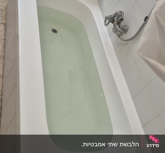 אמבטיה לבנה עם מים, ברז ומקלחת בחדר רחצה